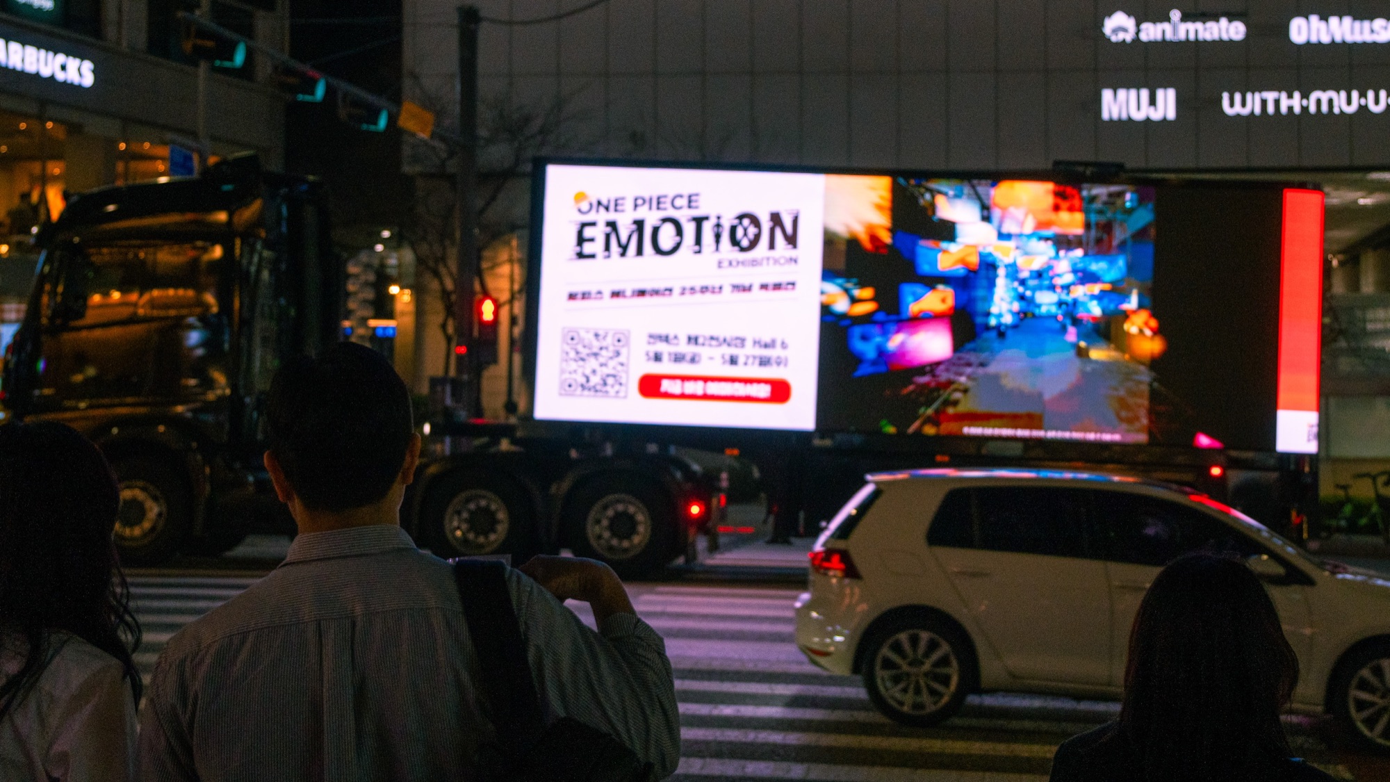 횡단보도 보행자 너머로 원피스 이모션 전시 영상을 보여주는 LED 트럭